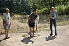 Flere voksne spiller petanque på en grusplads en solrig dag.
