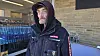 Mand i mørkt overtøj står foran supermarked med vandflasker stablet ved indgangen.