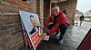 Mand i rød jakke ordner stakke af røde valgplakater op ad en mur på en våd fortovsgade.