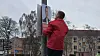 Mand i rød jakke hænger socialdemokratisk valgplakat op på en lygtepæl i bymiljø.