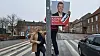 Person hænger Socialdemokratiet valgplakat på lygtepæl ved fodgængerfelt på grå regnvejrsdag.