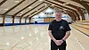 Søren Hansen, Ravnsborghallen, står i den tomme idrætshal med træloft og tilskuerpladser i siden.