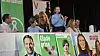 Panel af politikere ved lang bord med partiplakater under en debat på en scene.