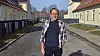 Ældre mand står på stille vej mellem gule bygninger med røde tage i solskin. Kjeld Saul.
