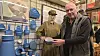 Mand i museum viser blåt emaljekøkkenudstyr ved siden af mannequin i uniform.
