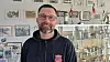 Mand i klubtrøje står foran glasmontre med pokaler og historiske fotos i en roklub.