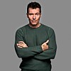 Portræt af mand i mørkegrøn trøje med korslagte arme foran grå baggrund.