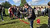 Mand med saks ved rød snor, mens en gruppe mennesker ser på ved en udendørs ceremoni.