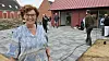 Smilende kvinde står foran en nyanlagt plads med fliser, planter og flere personer ved et pakhus.
