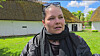 Kvinde foran hvide stråtækte bygninger og grønne marker i dagslys.