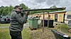 Mand i grøn jakke sigter med et gevær ved et udendørs skydeområde.