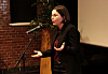 Signe Byrge Sørensen taler ved en mikrofon i en sal med lærred og murstensvæg.