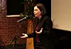 Signe Byrge Sørensen taler ved en mikrofon i en sal med lærred og murstensvæg.