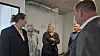 Fire personer taler sammen i et lyst lokale med industrielle loftsdetaljer.