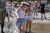 To kvinder står i vandet ved et springvand til en udendørs festival, mens folk ser til i baggrunden.
