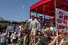 Personer samles ved en rød scene med bannere og skilte til en udendørs demonstration.