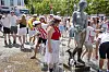 Folk står omkring en sølvfarvet menneskestatue ved et springvand i en bypark.