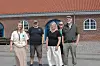 Fire personer står foran en rød murstensbygning med rødt tegltag.