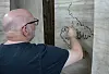 En mand tegner på et stort papirark ophængt på en væg.