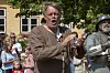 Mand i brun dragt optræder foran tilskuere ved et historisk arrangement i en gårdhave.