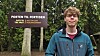 Ung besøgende foran et skilt i en grøn skov.