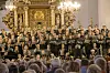 Stort kor synger i en udsmykket kirke, mens en dirigent står foran publikum.