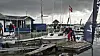 Sejlere ved bådebroen i en marina med mindre både, master og flag.