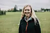 Smilende kvinde i mørk jakke står foran grønne marker.