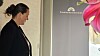 Kvinde i profil foran et gråt skilt med lyserøde blomster i højre side.