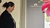 Kvinde i profil foran et gråt skilt med lyserøde blomster i højre side.