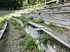 Forfaldne trætribuner med bænke og grøn vegetation i et udendørs område.