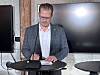 Mand i ternet blazer ved et podium foran store skærme.
