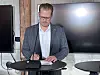 Mand i ternet blazer ved et podium foran store skærme.