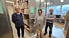 Tre personer står sammen i et moderne lokale med skærme og teknisk udstyr.
