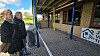 To personer står ved en overdækket indgang til en murstensbygning med skiltning.