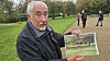 Ældre mand viser et indrammet fotografi i en grøn park.